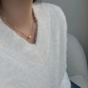 Polished gold heart pendant on a fine link chain worn over a white knit sweater