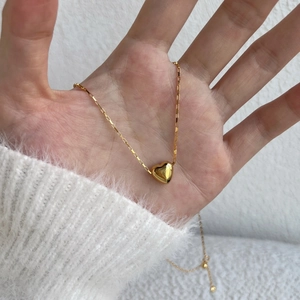 Detail of a polished 3D heart pendant on a gold box chain held against white knitwear
