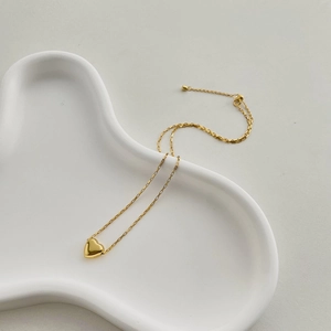 Macro detail of a polished gold heart pendant on a minimalist rectangular link chain