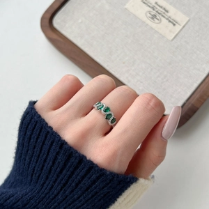 Macro shot of silver wave ring with green oval zircons and white stones on finger
