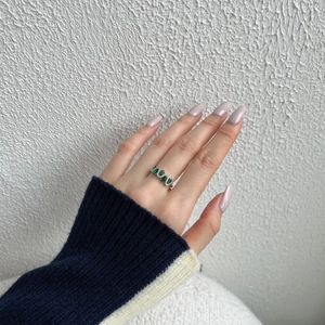 Detailed view of wave-shaped S925 silver ring with green marquise stones on a model's hand