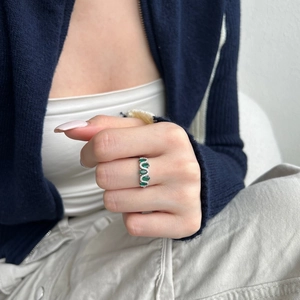 Close-up of S925 silver wave ring with green oval zircon stones on a model's finger