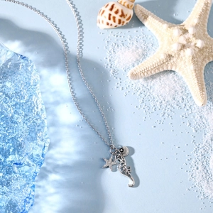 Detail of silver marine necklace with seahorse, starfish, and shell pendant on beach sand
