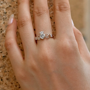 Classic silver Claddagh ring with heart-shaped zircon on finger against a stone wall