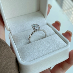 Dettaglio anello in zircone taglio ovale con halo nascosto e pavé in scatola regalo bianca