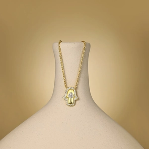 Vue détaillée du pendentif main de Hamsa doré serti de zircons sur un vase