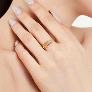 Détail d'une bague trombone dorée avec des pierres précieuses rectangulaires colorées