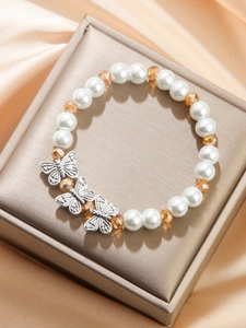 Detail of beaded pearl bracelet featuring silver butterfly charms on silk fabric
