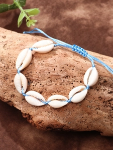 Close-up of handmade cowrie shell anklet with sky blue woven cord on wood display