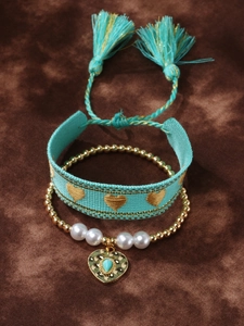 Detail of bohemian heart charms on turquoise woven strap and gold beaded pearl bracelets