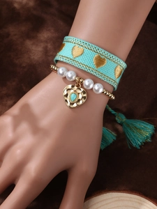 Detail of bohemian teal heart bracelet set with golden embroidery, tassel, and stone pendant