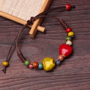 Handmade woven ceramic bracelet with red heart bead on vintage wood background