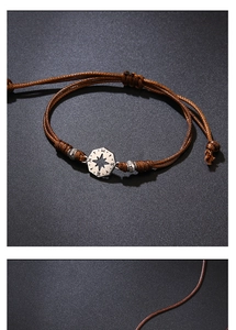 Macro detail of brown woven bracelet featuring a vintage silver compass charm with NSEW engraving