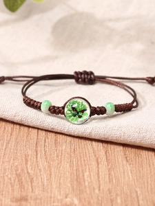 Detail of hand-woven cord bracelet with green butterfly glass bead and ceramic charms