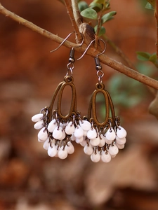Close-up of bohemian bronze earrings with white teardrop tassels hanging on a wood branch