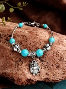 Detailed view of turquoise bead bracelet with owl charm on vintage wood and fabric