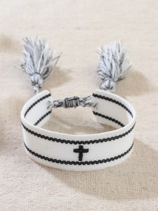 Dettaglio del bracciale intrecciato bianco con croce nera e frange su juta naturale