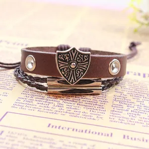 Vintage leather layered bracelet with cross shield charm and rivet details on old newsprint