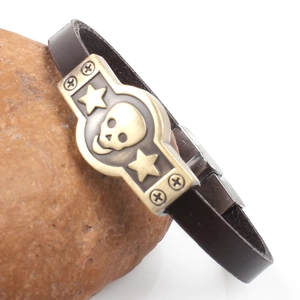 Punk skull brown leather bracelet with bronze alloy emblem on a natural rock