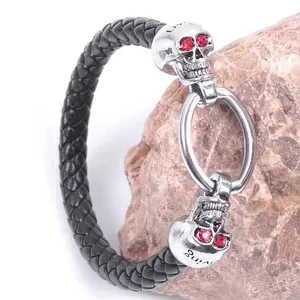 Punk woven black leather bracelet with silver skulls and red rhinestone eyes on a rock