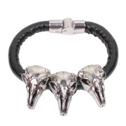 Close-up of punk style braided leather bracelet with three metallic silver skulls