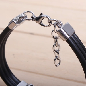 Macro shot of three-strand black cord bracelet featuring a silver lobster clasp and chain