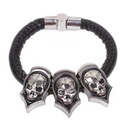Close-up of black braided leather punk bracelet featuring three silver skull charms