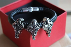 Detail of punk leather bracelet with silver skull charms on a red gift box display