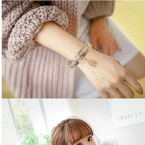 Multilayer leather wrap bracelet with metallic tassel charms on a warm knit sweater