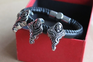 Detail of black braided leather bracelet with three silver skull metal charms on red gift box
