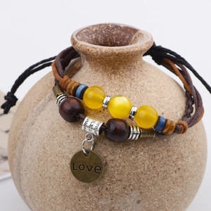 Handmade woven wax rope bracelet with yellow crystal beads and Love charm on ceramic vase