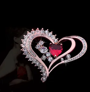 Détail d'une broche double cœur en or rose avec pierre rouge et cristaux sur fond noir