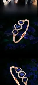 Close-up of rose gold open bangle featuring three deep blue oval crystals and zircons