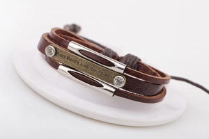 Détail d'un bracelet en cuir vintage avec plaque métallique gravée sur fond blanc