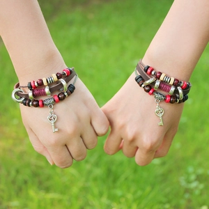 Close-up of multilayer leather bracelet featuring vintage key pendant on grass background
