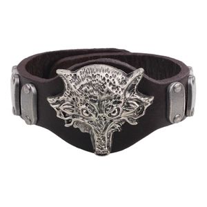 Detail of a brown leather bracelet with a carved metal wolf head and decorative studs