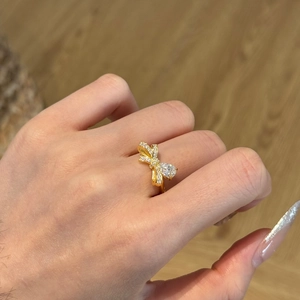 Dettaglio anello a fiocco dorato con pietra a goccia e pavé di zirconi indossato sulla mano