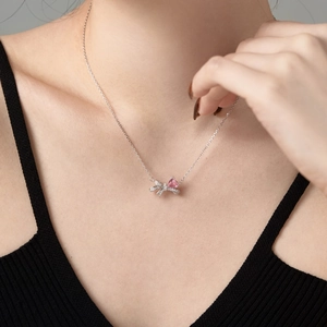 Nahaufnahme einer S925 Silberkette mit rosa Herz-Edelstein und Schleifenanhänger am Modell