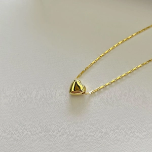 Macro shot of 925 silver golden heart pendant with polished surface on white texture