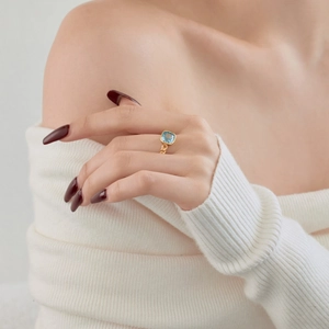 Detail of square blue gemstone ring with gold chain-link band on a model hand