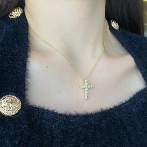 Dettaglio di una collana con ciondolo a croce dorata con zirconi cubici su una modella