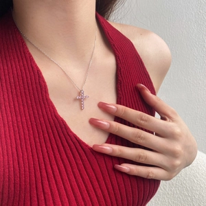 Dettaglio del ciondolo a croce in argento S925 con zirconi rosa su una modella donna