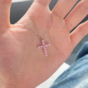 Dettaglio del ciondolo a croce in argento con pietre di zirconi rosa sul palmo della mano