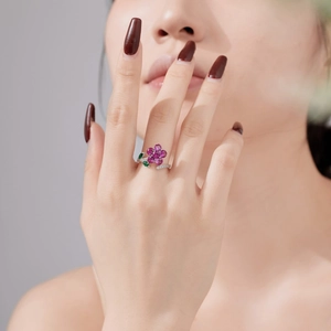 Detail van S925 zilveren bloemring met roze bloemblaadjes en groene bladeren aan vinger