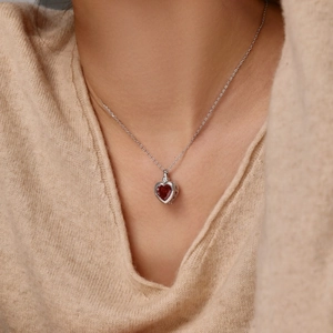 Detail of a red heart-shaped gemstone pendant with a delicate silver chain on a beige sweater