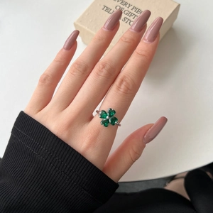 Detail of clover ring with heart-shaped green zircons worn on finger with pink nails