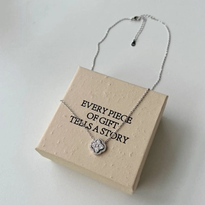 Vue détaillée du collier trèfle argenté avec zircons posé sur un coffret cadeau