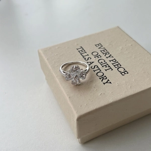Macro detail of silver four-leaf clover ring with heart-shaped cubic zirconia in a gift box
