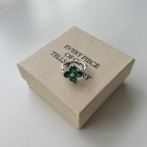 Détail de bague trèfle en argent avec zircons verts sur boîte cadeau texturée