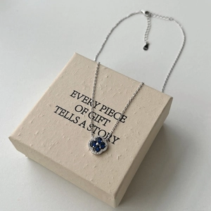 Détail macro du collier en argent S925 avec pendentif trèfle bleu sur une boîte cadeau